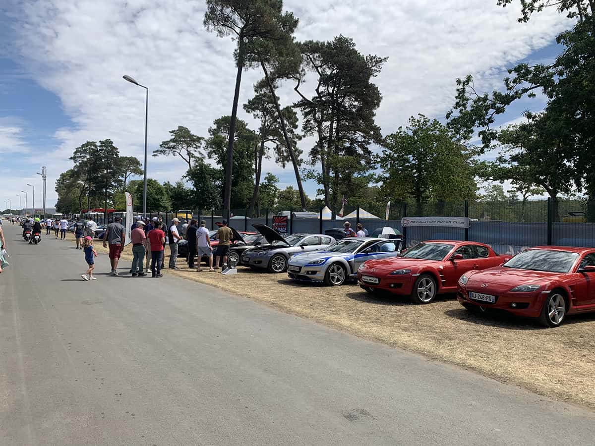 Visiteurs posant des questions devant les Mazda RX du Révolution Rotor Club sur l’aire clubs du Mans Classic 2025.