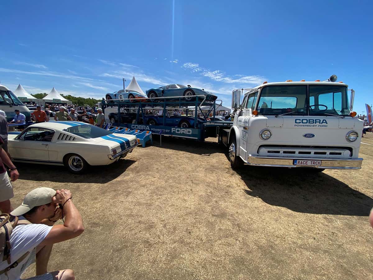 Camion Ford blanc chargeant des GT40 Gulf, foule et ciel bleu au Mans Classic 2025.