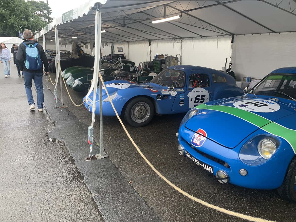 Prototypes bleus Alpine/René Bonnet alignés sous bâche, sol détrempé, Mans Classic 2025