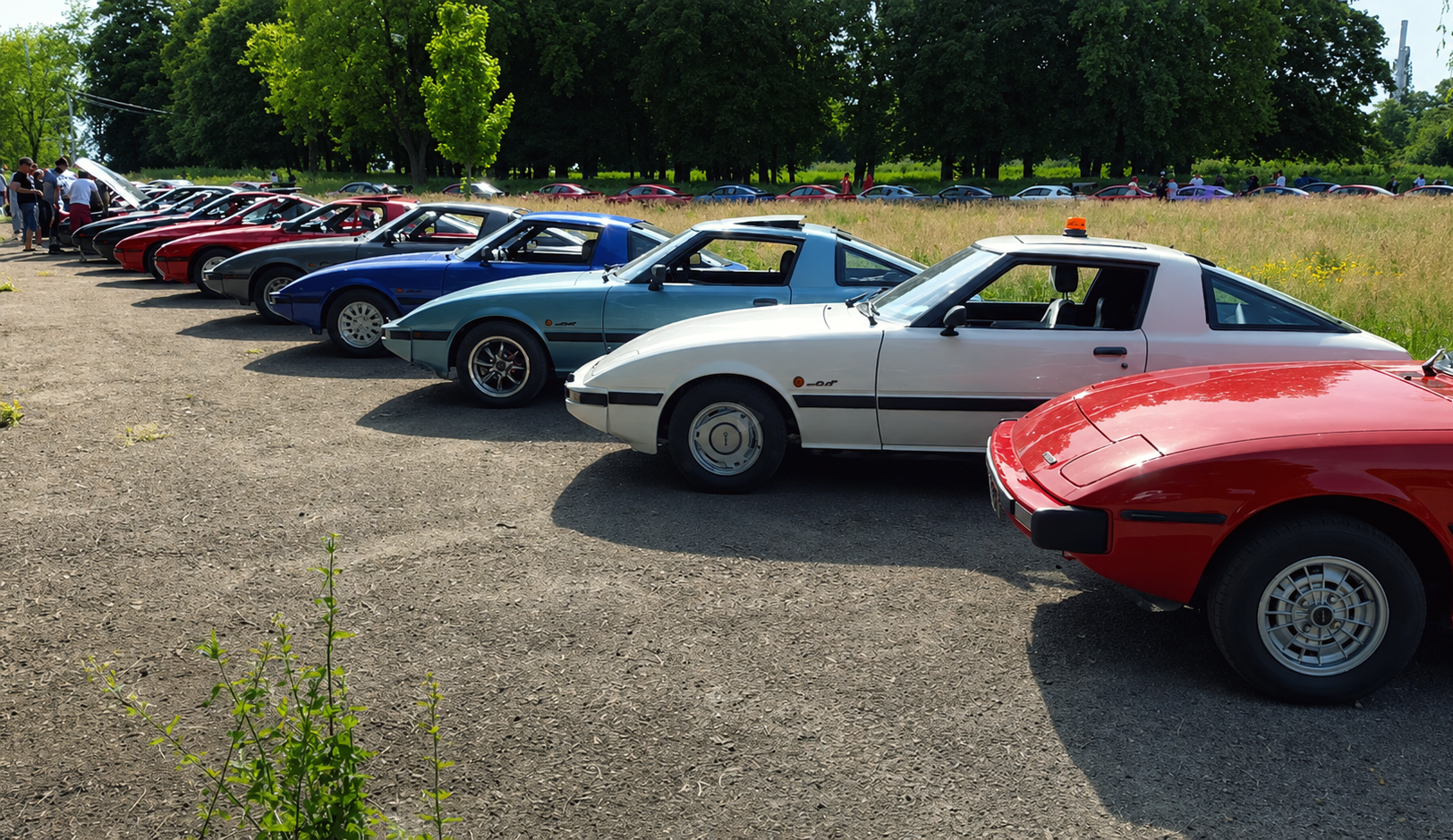 Classic Rotary Day 2026 - les RX-7 SA22 et FB en formation sur l'aérodrome de Niergnies Rangée de Mazda RX-7 SA22 et FB alignées sur l'aérodrome de Niergnies lors du Classic Rotary Day 2026 - SA22 rouge au premier plan, SA22 blanche, FB bleue et FB verte silver en arrière-plan, rangée de RX-8 visible au loin