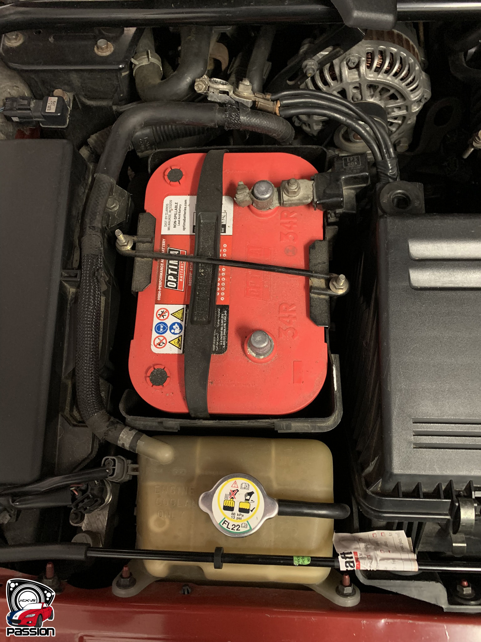 Batterie Optima rouge en place dans le compartiment moteur d'une Mazda RX-8 avec cosse n&eacute;gative &agrave; d&eacute;brancher